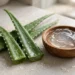 Aloe vera leaves beside a bowl of clear aloe gel on a stone surface