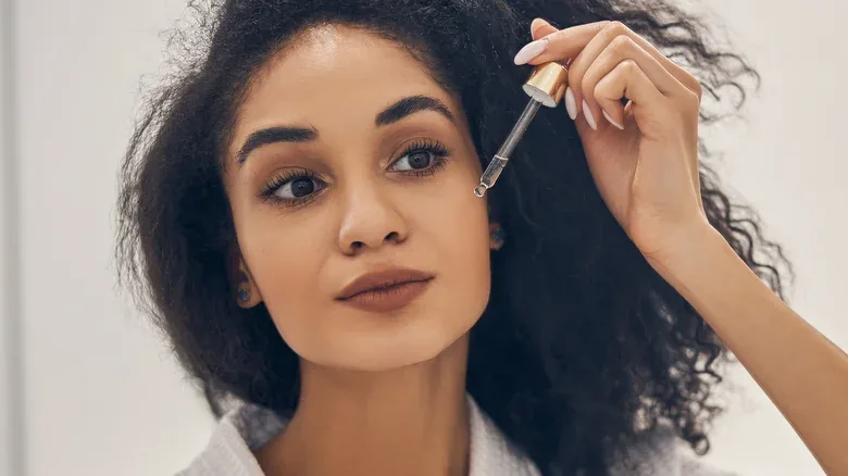 Close-up of a woman holding a serum dropper near her cheek