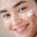 Woman with clear, glowing skin applying moisturizer as part of a daily skincare routine