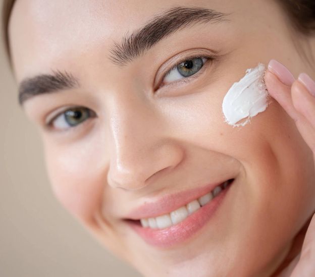 Woman with clear, glowing skin applying moisturizer as part of a daily skincare routine