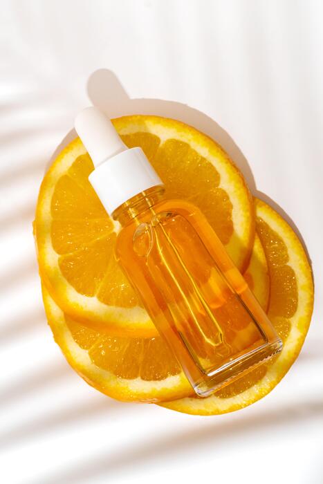 Serum dropper bottle with orange slices on a white background